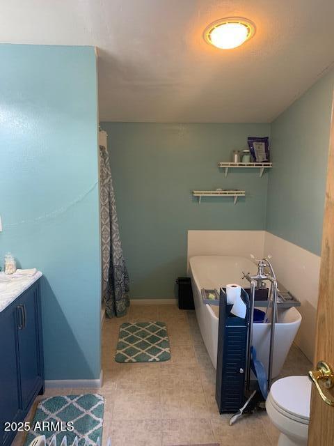 bathroom with toilet, a washtub, vanity, and baseboards