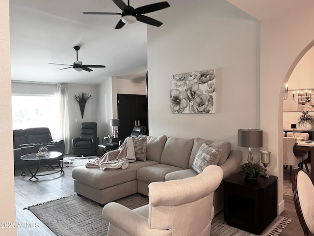 living area with arched walkways, ceiling fan, and wood finished floors