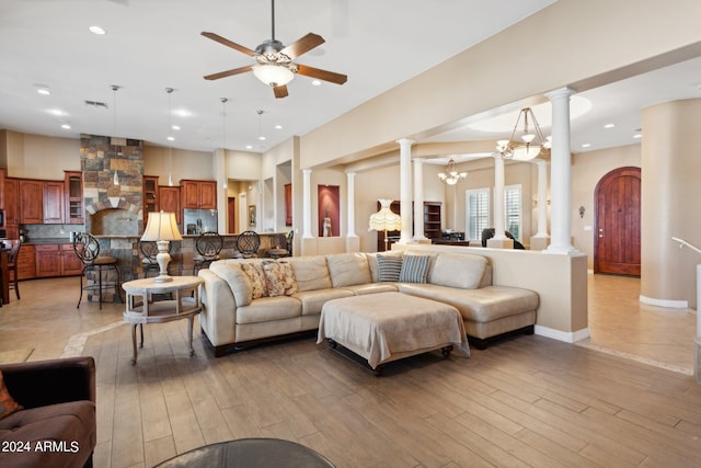 living room with ceiling fan with notable chandelier, light hardwood / wood-style floors, and ornate columns