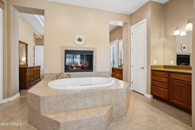 bathroom featuring a relaxing tiled tub, tile patterned flooring, a tile fireplace, and vanity