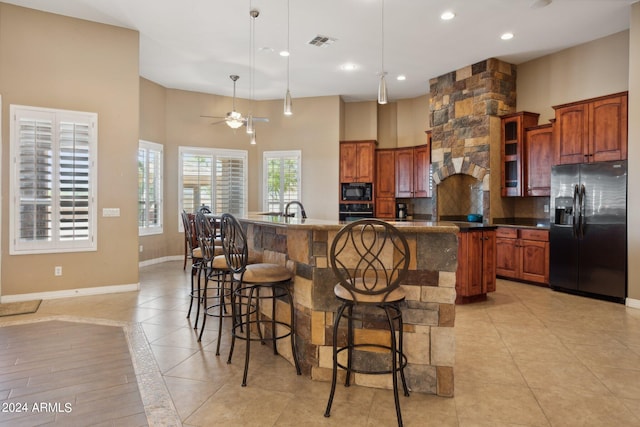 kitchen with a high ceiling, black appliances, ceiling fan, and a kitchen island with sink