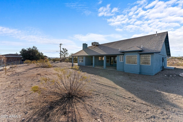 view of front of home with stucco siding, a patio, and roof with shingles