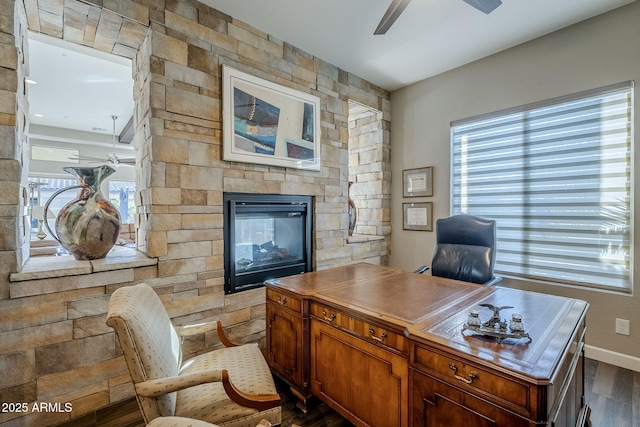 office area featuring dark hardwood / wood-style floors, a stone fireplace, ceiling fan, and a healthy amount of sunlight