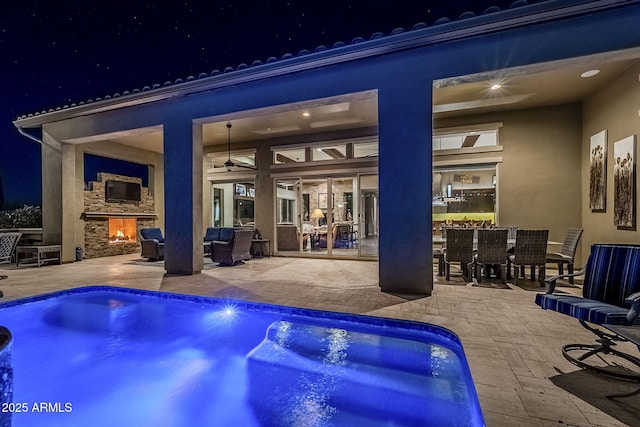 pool at night featuring an outdoor living space with a fireplace and a patio area