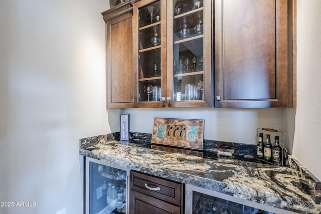 bar featuring dark stone countertops, dark brown cabinets, and beverage cooler