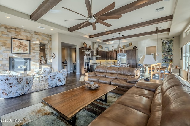 living room featuring ceiling fan, a fireplace, beamed ceiling, and dark wood-type flooring