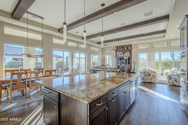 kitchen with decorative light fixtures, a healthy amount of sunlight, sink, and an island with sink