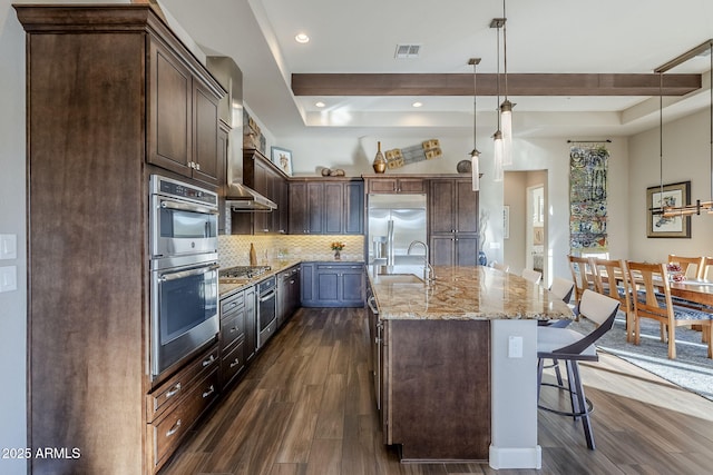 kitchen with light stone countertops, stainless steel appliances, tasteful backsplash, pendant lighting, and a kitchen island with sink