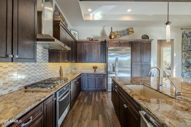 kitchen featuring sink, hanging light fixtures, wall chimney exhaust hood, tasteful backsplash, and stainless steel appliances