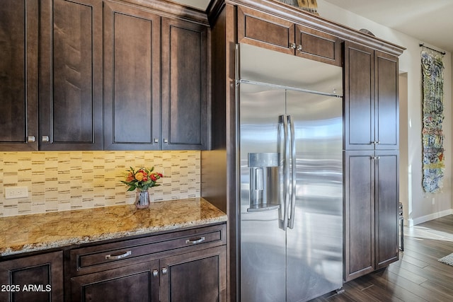 kitchen with dark wood-type flooring, light stone counters, backsplash, built in refrigerator, and dark brown cabinets