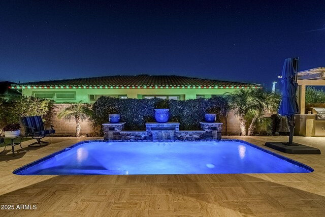 pool at night featuring a grill, pool water feature, and a patio