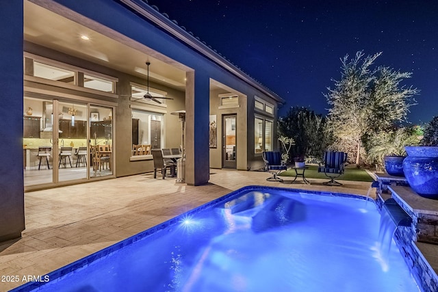 pool at twilight with pool water feature, ceiling fan, and a patio