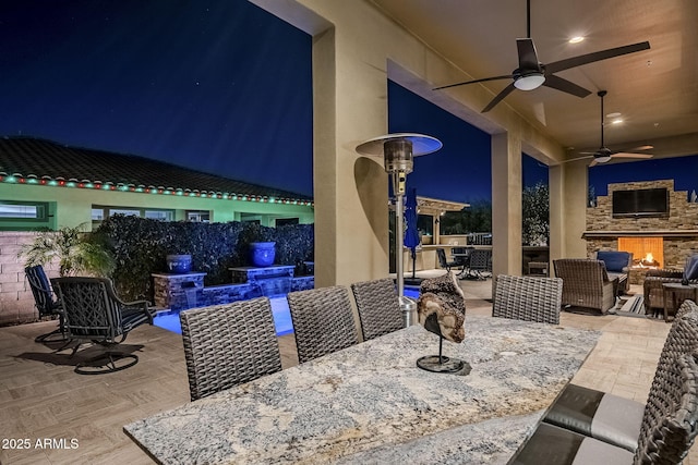 patio at twilight with an outdoor living space with a fireplace and ceiling fan