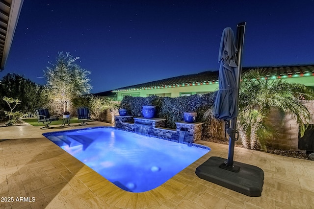 pool at night featuring pool water feature and a patio