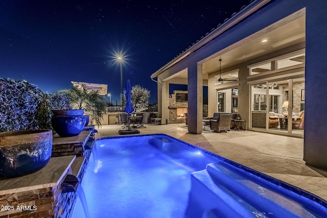 pool at night with pool water feature, an outdoor stone fireplace, and a patio