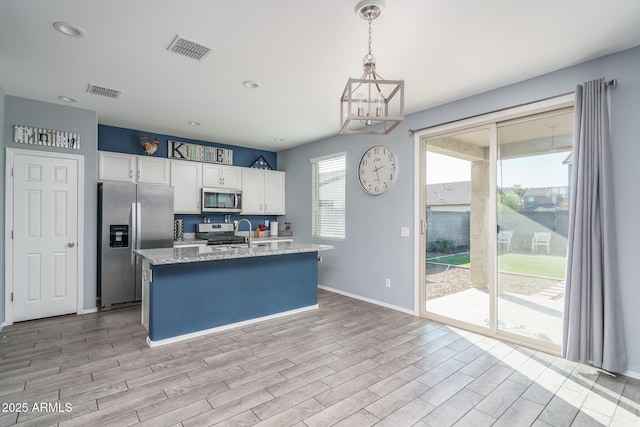 kitchen featuring light stone countertops, white cabinetry, pendant lighting, a center island with sink, and appliances with stainless steel finishes