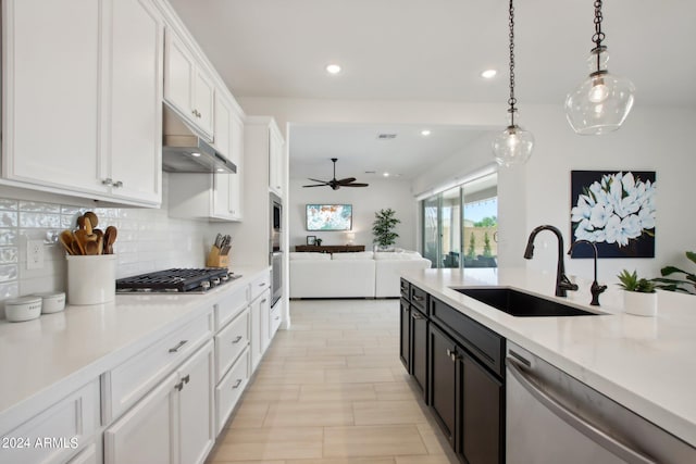 kitchen with appliances with stainless steel finishes, open floor plan, decorative light fixtures, white cabinetry, and a sink