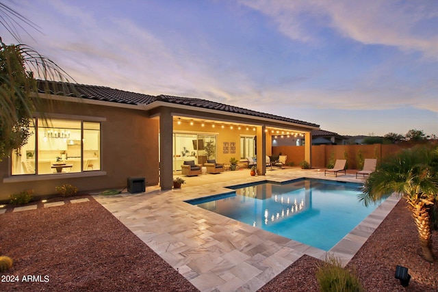 back of property at dusk with a fenced in pool, stucco siding, an outdoor hangout area, a patio area, and fence