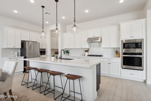 kitchen featuring under cabinet range hood, stainless steel appliances, a sink, white cabinetry, and light countertops