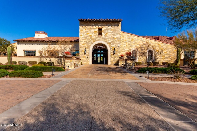 mediterranean / spanish house with stucco siding, a tile roof, stone siding, and french doors