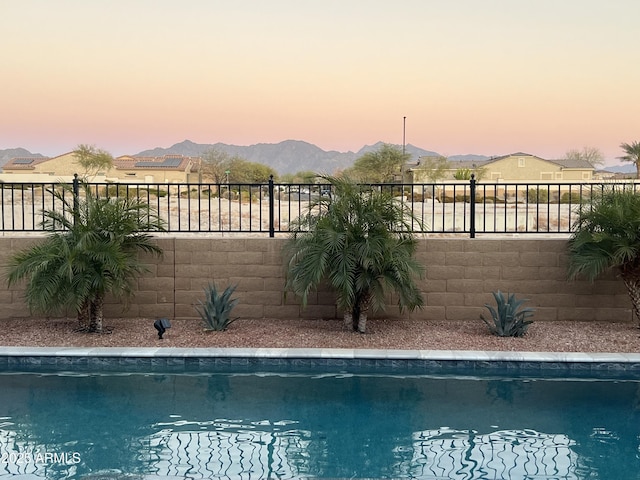 pool at dusk featuring fence, a mountain view, and a fenced in pool