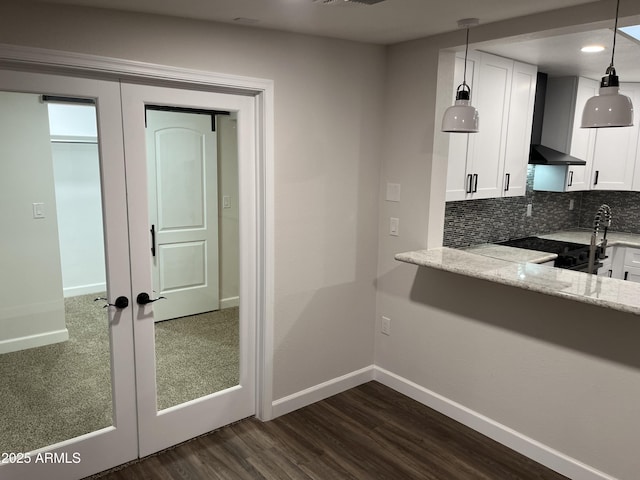 kitchen featuring light stone counters, white cabinets, french doors, wall chimney range hood, and backsplash