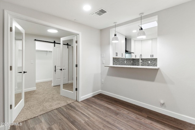 kitchen featuring a barn door, white cabinetry, visible vents, tasteful backsplash, and dark wood finished floors