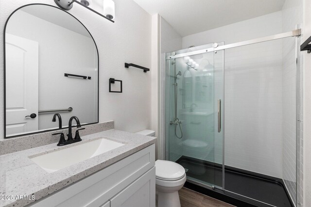 bathroom with vanity, a shower stall, toilet, and wood finished floors