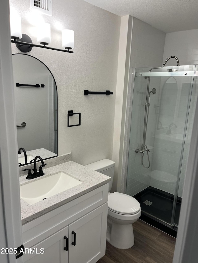 full bath featuring toilet, wood finished floors, a textured ceiling, vanity, and a shower stall