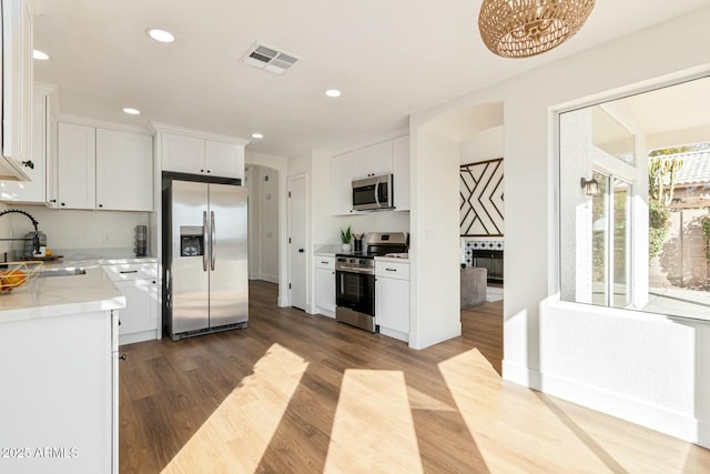 kitchen featuring light stone countertops, stainless steel appliances, sink, hardwood / wood-style floors, and white cabinetry