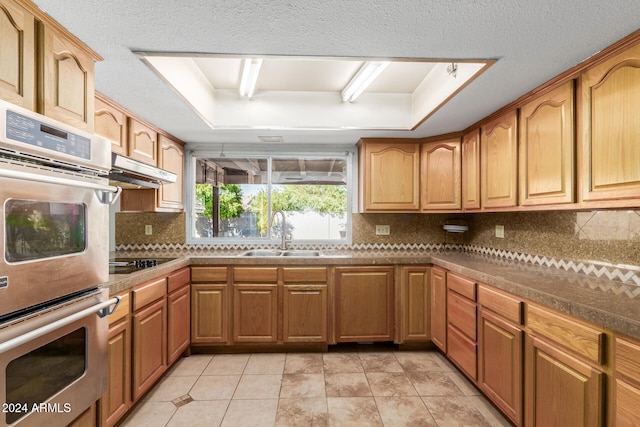 kitchen featuring sink, a raised ceiling, double oven, backsplash, and black electric stovetop