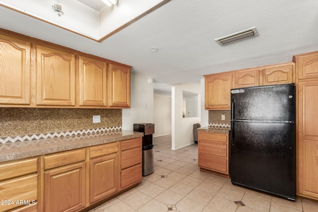 kitchen featuring decorative backsplash, black fridge, and light tile patterned flooring