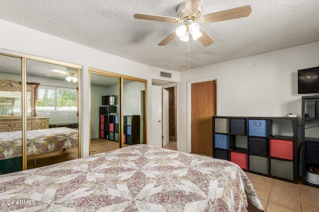 bedroom with ceiling fan, light tile patterned floors, a textured ceiling, and multiple closets