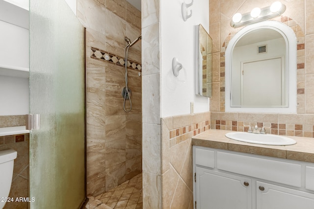 bathroom with toilet, vanity, tile walls, and tiled shower