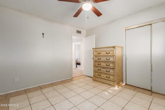 unfurnished bedroom featuring ceiling fan, a closet, light tile patterned floors, and a textured ceiling