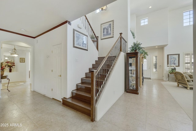 stairs with crown molding, tile patterned floors, and a towering ceiling