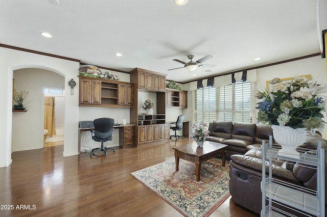 living room featuring dark hardwood / wood-style flooring, built in desk, ornamental molding, and ceiling fan