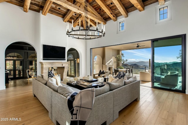 living area featuring arched walkways, wood ceiling, light wood-style floors, beam ceiling, and a high end fireplace