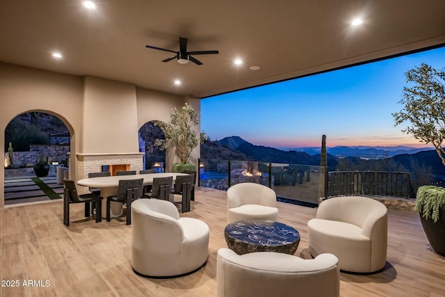 wooden terrace featuring a mountain view, a lit fireplace, and a ceiling fan