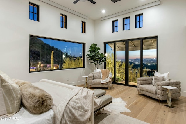 bedroom with baseboards, light wood-style flooring, access to exterior, a high ceiling, and a mountain view