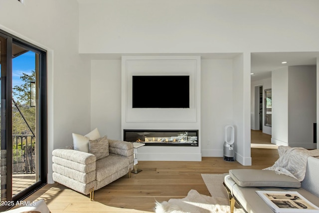 living area with a glass covered fireplace, light wood-style flooring, baseboards, and recessed lighting