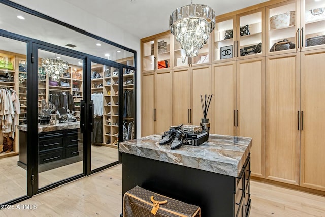 walk in closet featuring light wood-type flooring and an inviting chandelier