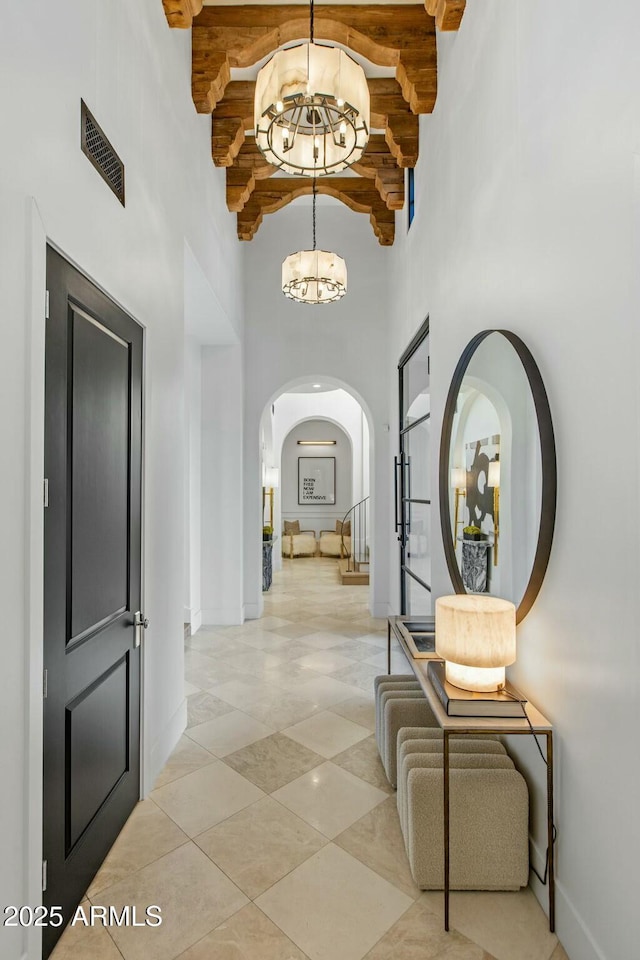 hall featuring visible vents, arched walkways, baseboards, stairs, and a chandelier