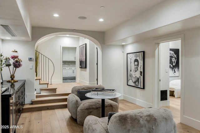 living area with light wood-style floors, visible vents, arched walkways, and recessed lighting