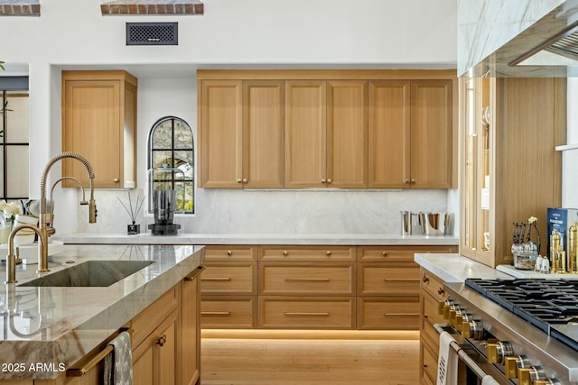 kitchen with stainless steel range, visible vents, backsplash, a sink, and light stone countertops