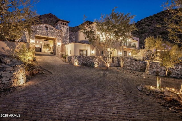 mediterranean / spanish home featuring a mountain view, a balcony, stone siding, decorative driveway, and stucco siding