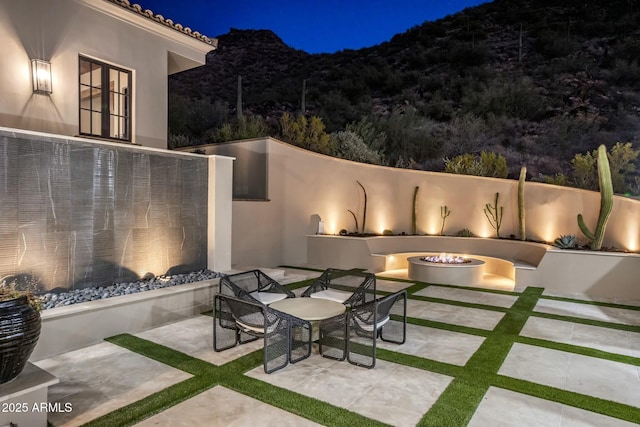 patio at twilight with a fire pit, a mountain view, and exterior fireplace