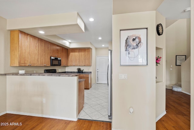 kitchen featuring light wood finished floors, a peninsula, recessed lighting, freestanding refrigerator, and black stove