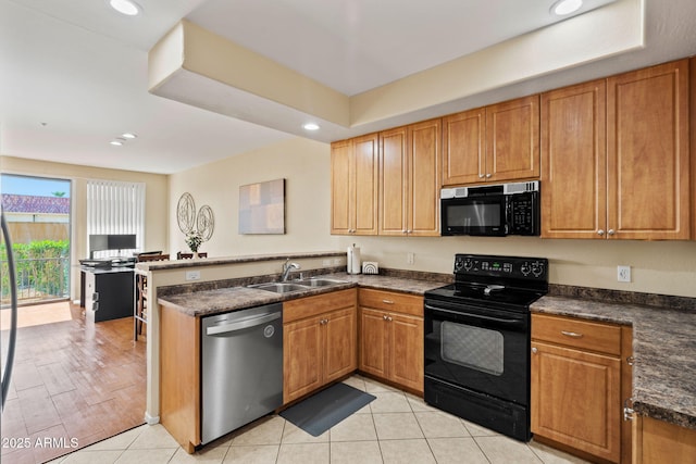 kitchen with recessed lighting, a peninsula, brown cabinetry, black appliances, and a sink