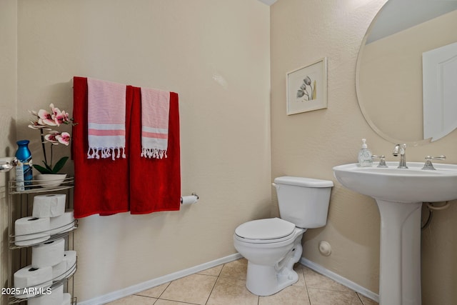 half bath featuring tile patterned flooring, toilet, baseboards, and a sink